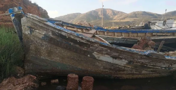 Un barco viejo y oxidado abandonado en la orilla de un mar contaminado, rodeado de basura, minerales y aguas turbias