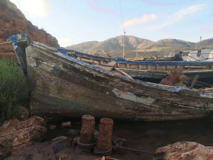 Un barco viejo y oxidado abandonado en la orilla de un mar contaminado, rodeado de basura, minerales y aguas turbias