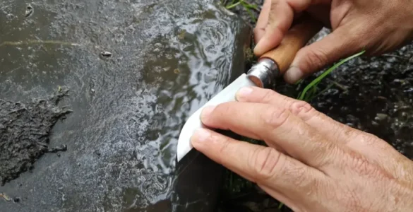 Primer plano de unas manos afilando una navaja sobre la piedra de una antigua calzada