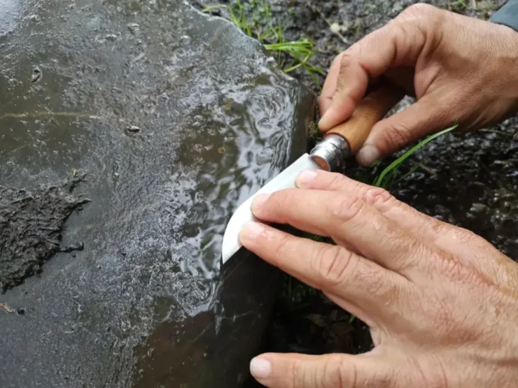 Primer plano de unas manos afilando una navaja sobre la piedra de una antigua calzada