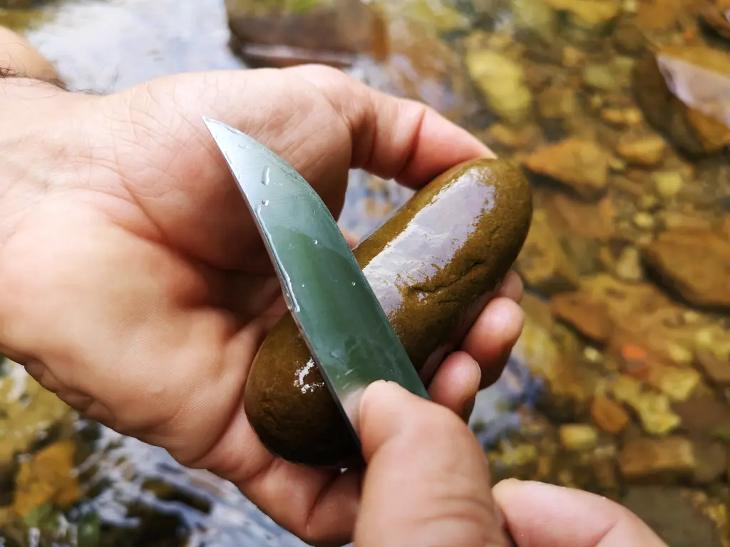 Primer plano de una mano afilando una navaja con un canto rodado del río Nansa