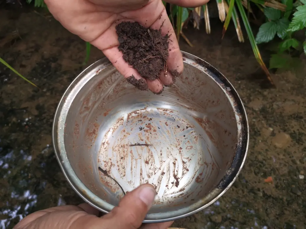 Primer plano de una olla sucia, con el borde quemado antes de fregarla sin jabón, con tierra y agua de río