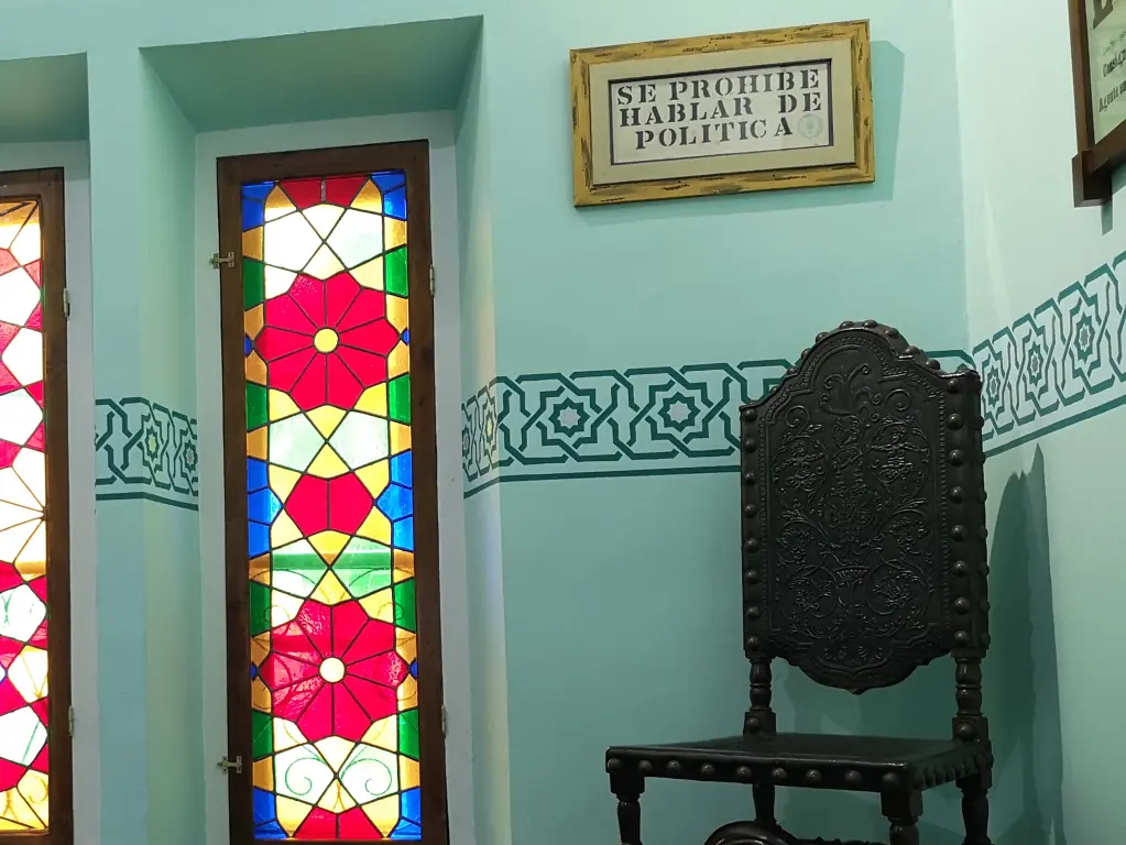 Interior de Quinta Guadalupe, Colombres. Se ve una silla, una vidriera y un cartel que avisa: se prohíbe hablar de política