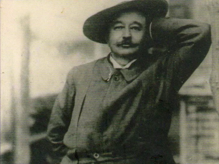 Retrato en blanco y negro de Iñigo Noriega Laso. Lleva un sombrero, el codo apoyado en un muro y sonríe a la cámara