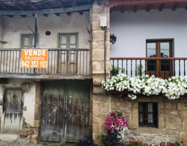 Casa antigua por restaurar con un cartel "se vende" a lado de una casa vacacional en el pueblo de Bárcena Pie de Concha