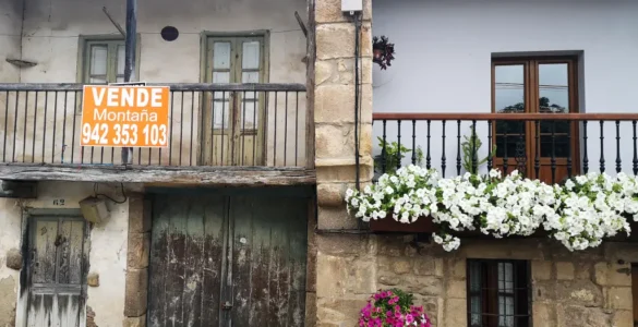 Casa antigua por restaurar con un cartel "se vende" a lado de una casa vacacional en el pueblo de Bárcena Pie de Concha