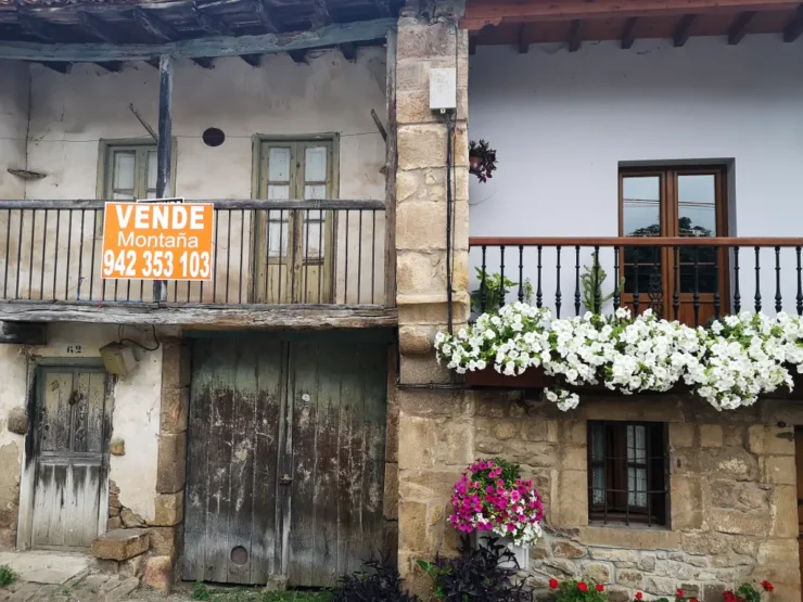 Casa antigua por restaurar con un cartel "se vende" a lado de una casa vacacional en el pueblo de Bárcena Pie de Concha