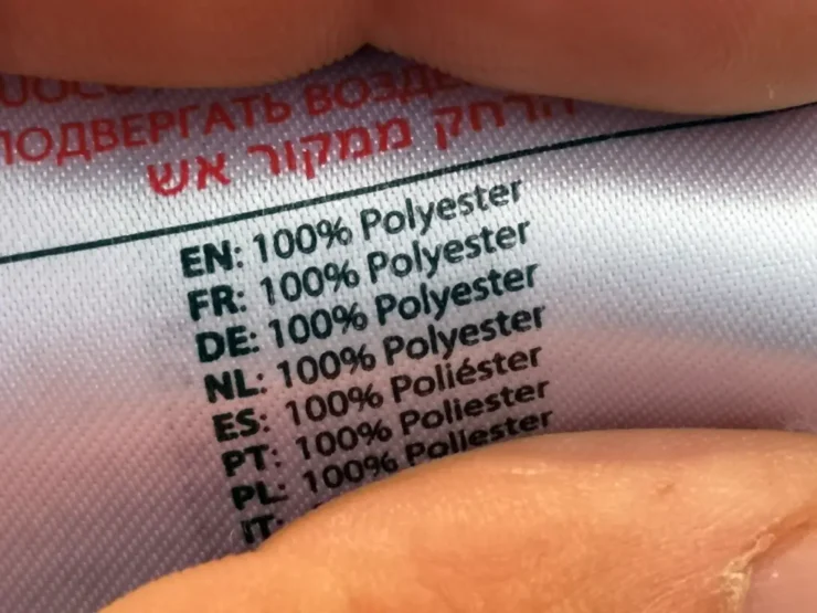 Primer plano de una etiqueta de ropa 100% poliester entre dos dedos