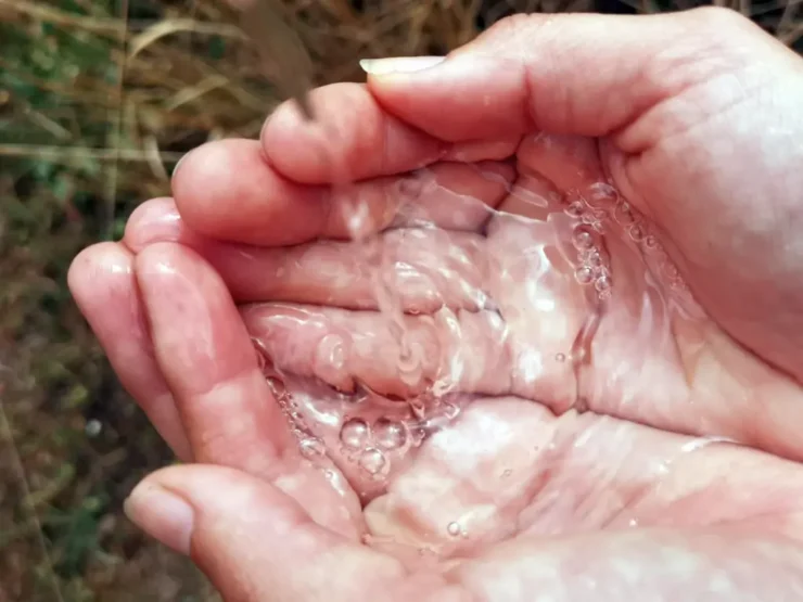 Dos manos juntas recogen agua goteando de una fuente