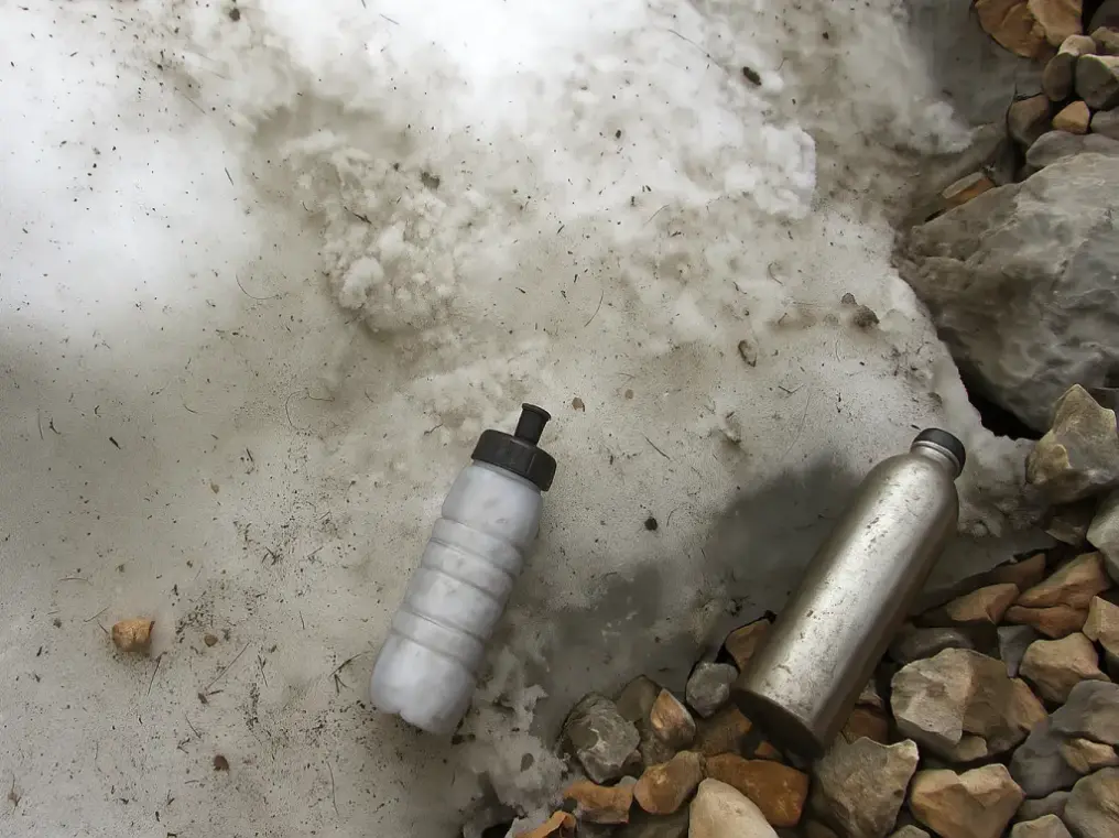 Dos botellas apoyadas al lado de un nevero. Una es transparente y está llena de nieve