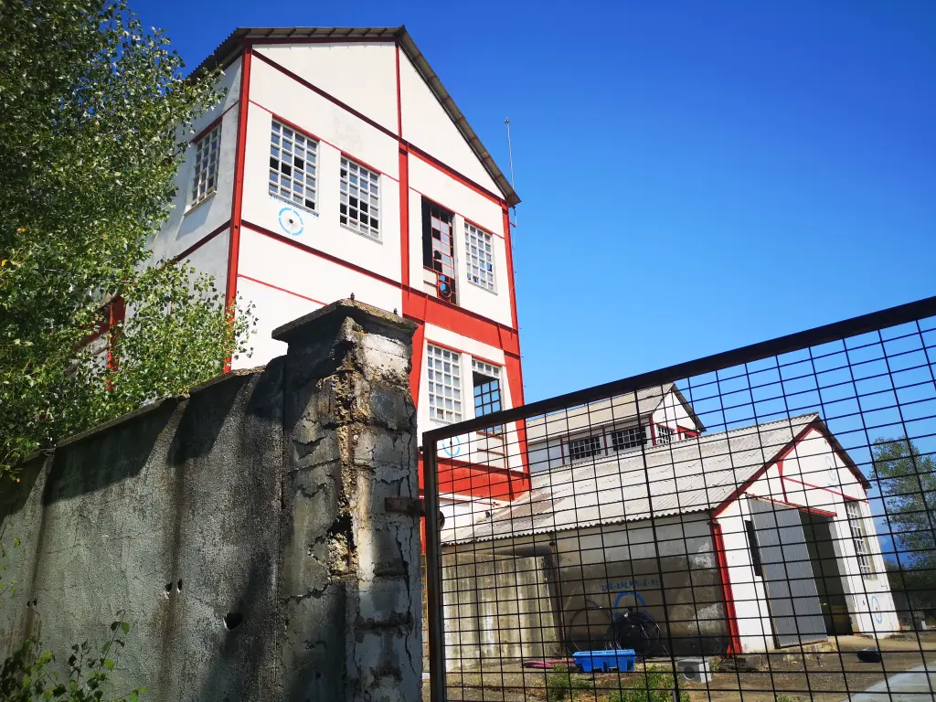 Reja de la cancela de entrada de la fábrica abandonada de Inquinosa S.A. con edificios al fondo