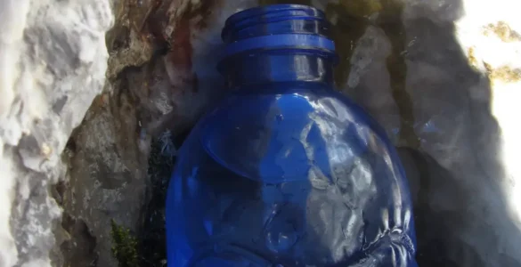Una botella de plástico recoge agua que brota de la roca