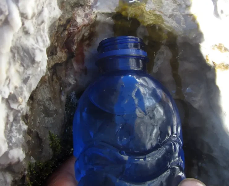 Una botella de plástico recoge agua que brota de la roca