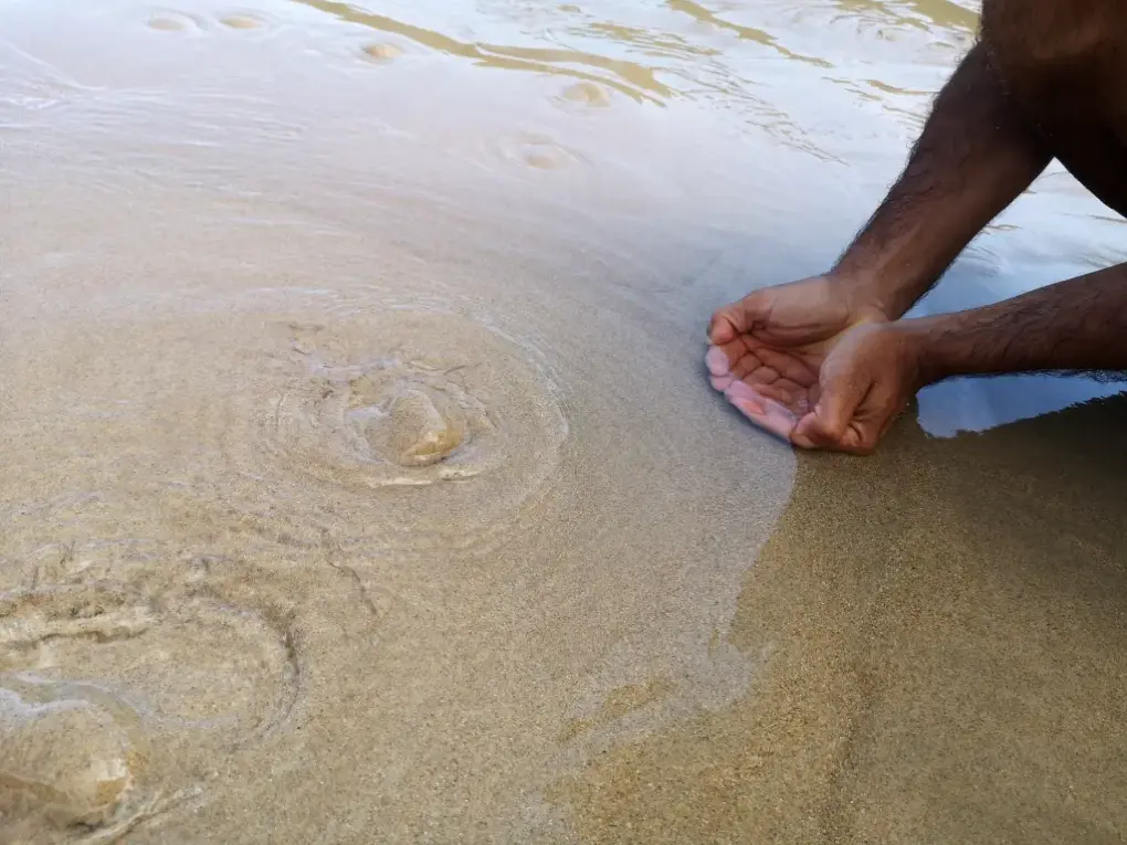 Manos juntas recogiendo agua de un manantial que brota del subsuelo, en este caso la arena de una playa