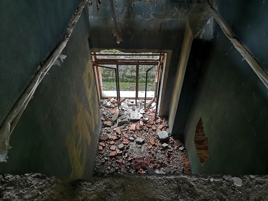 Sanatorio abandonado de Tablada: gran abertura vertical desde la segunda planta, con escombros y entrada secundaria sin vidrios al jardín
