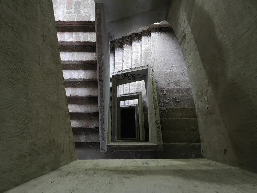 Sanatorio abandonado de Tablada: escaleras visibles a través del hueco que conecta todas las plantas, con oscuridad al fondo