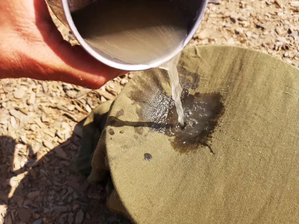 Mano vertiendo agua turbia a través de un pañuelo para filtrarla dentro de una olla antes de potabilizarla