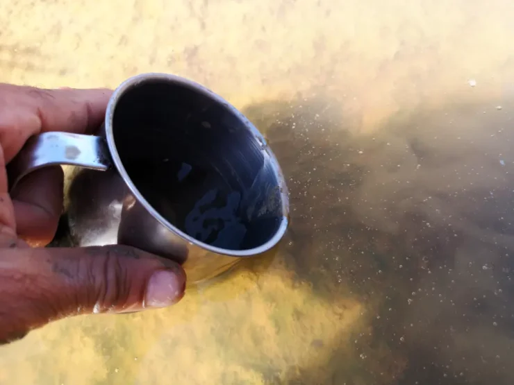 Mano recoge agua turbia del arroyo Pedraza con una taza de metal antes del proceso de filtrado y potabilización