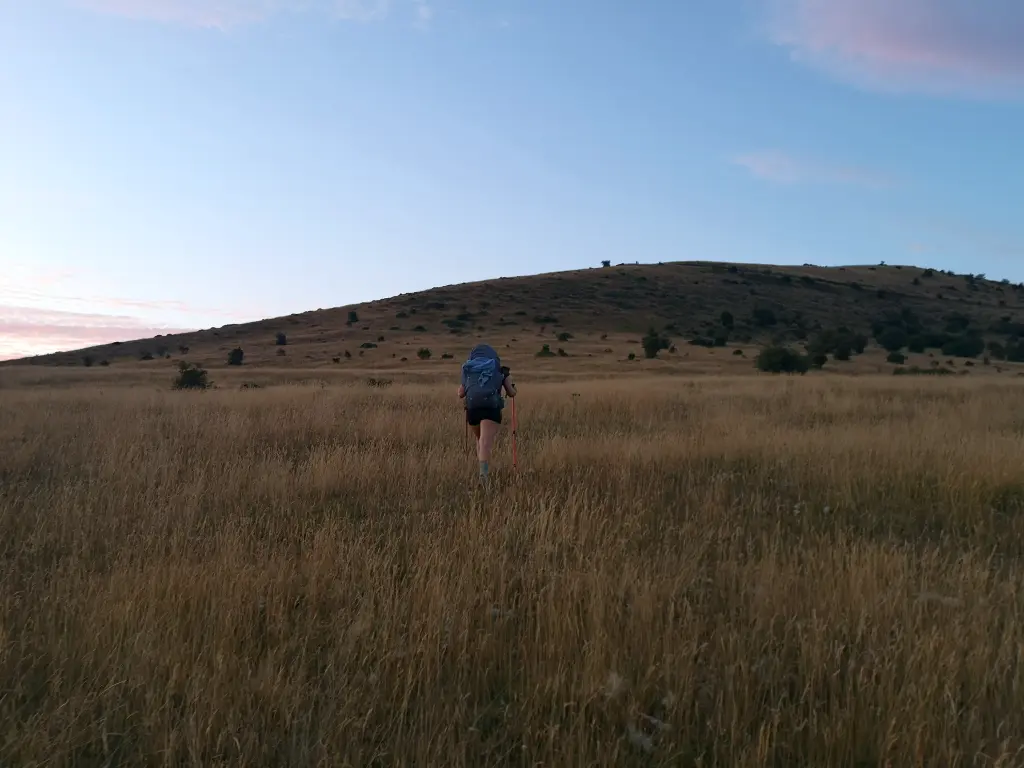 Viajera cruzando una cuesta campo a través, orientándose con el sol al atardecer