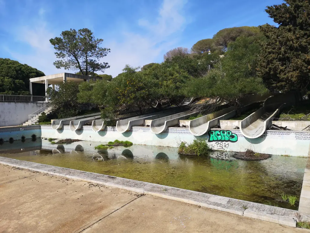 Piscina de aterrizaje de los toboganes principales del parque acuático abandonado en Castro Marín, Portugal, con el vaso vacío, superficies deterioradas y evidentes signos de abandono y falta de mantenimiento.